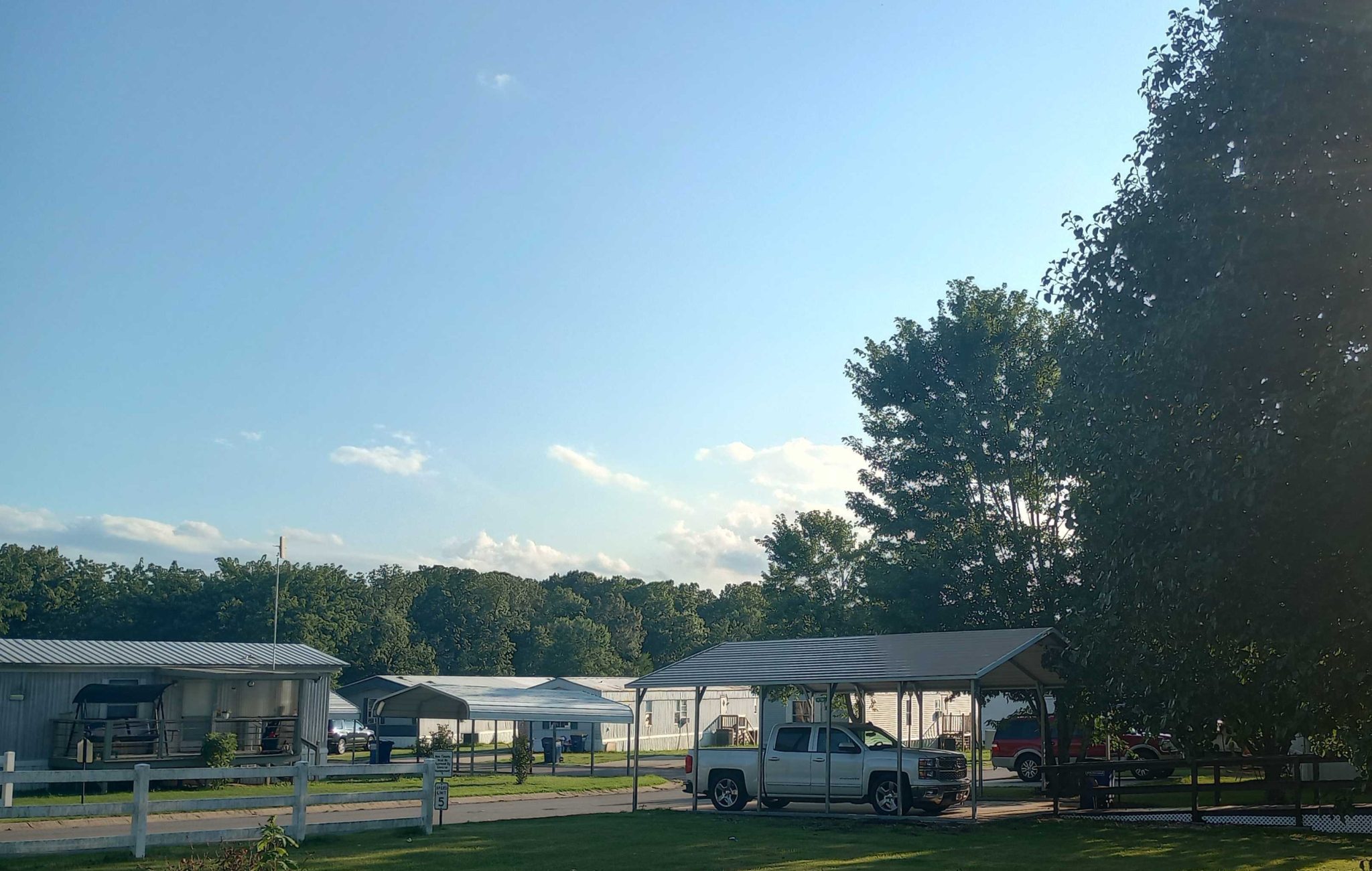 A road in Glenbriar Mobile Home Park during autumn, lined with mobile homes, green lawns, and colorful trees.