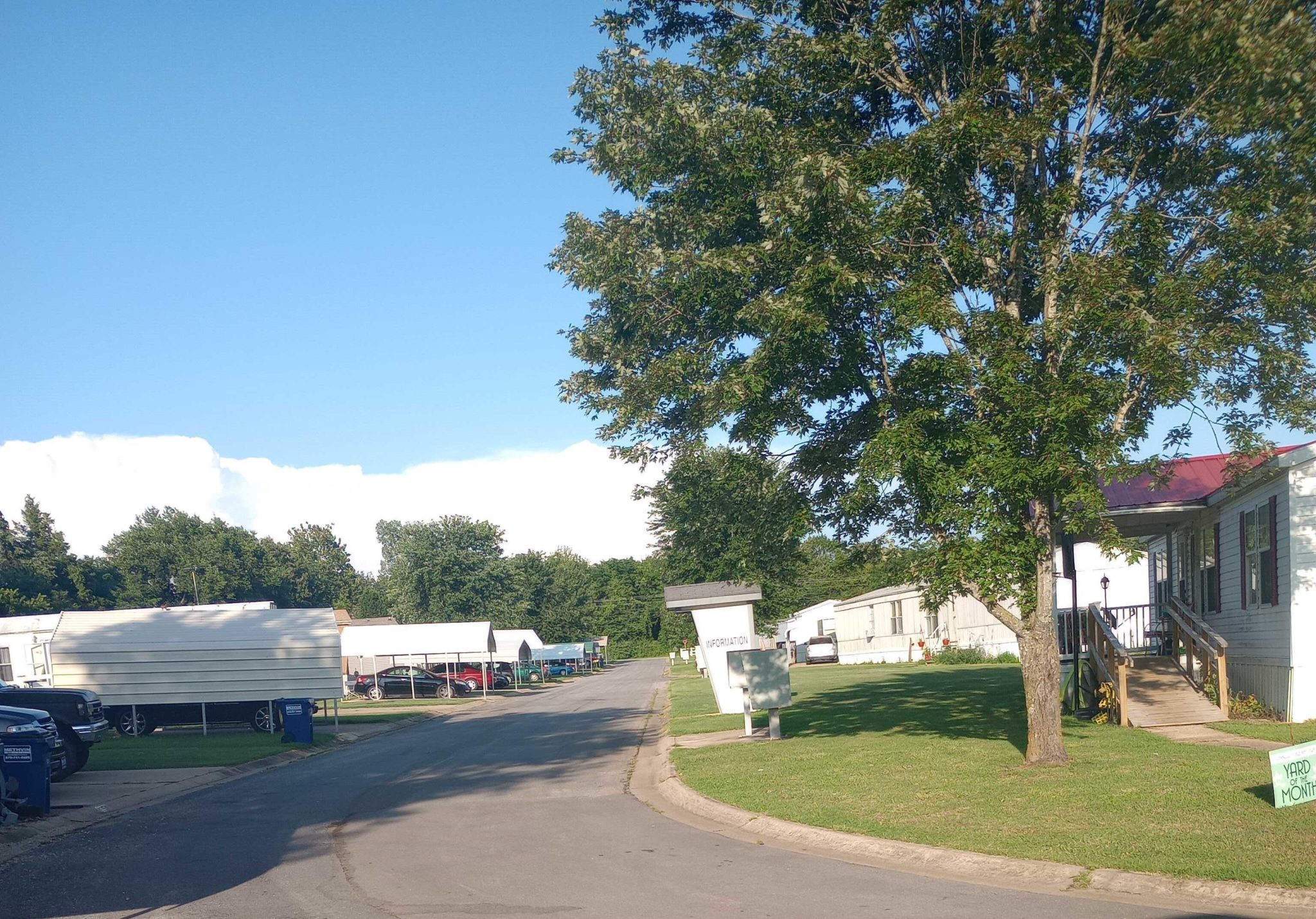 A road in Glenbriar Mobile Home Park during autumn, lined with mobile homes, green lawns, and colorful trees.