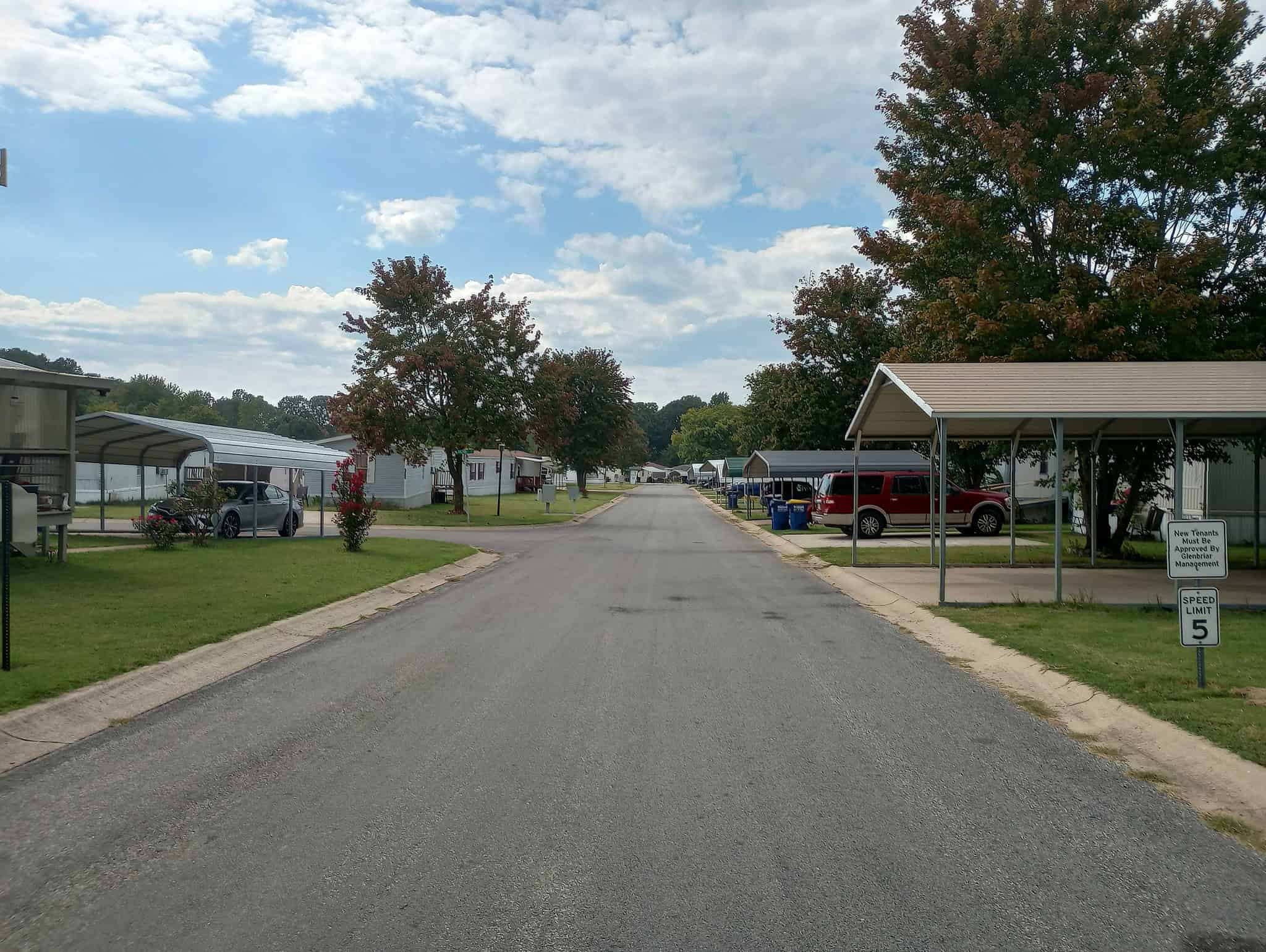 A road in Glenbriar Mobile Home Park during autumn, lined with mobile homes, green lawns, and colorful trees.