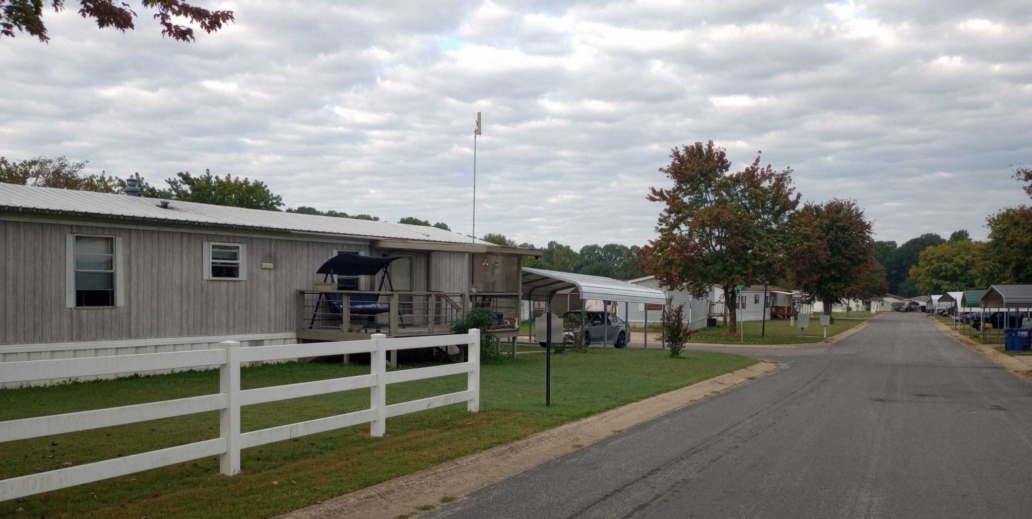 A road in Glenbriar Mobile Home Park during autumn, lined with mobile homes, green lawns, and colorful trees.