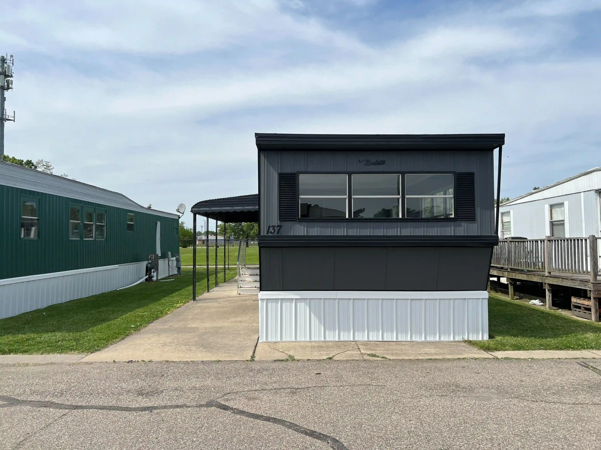Newly renovated mobile home at Roseville Mobile Home Park with fresh paint and a tidy lawn, under a partly cloudy sky.