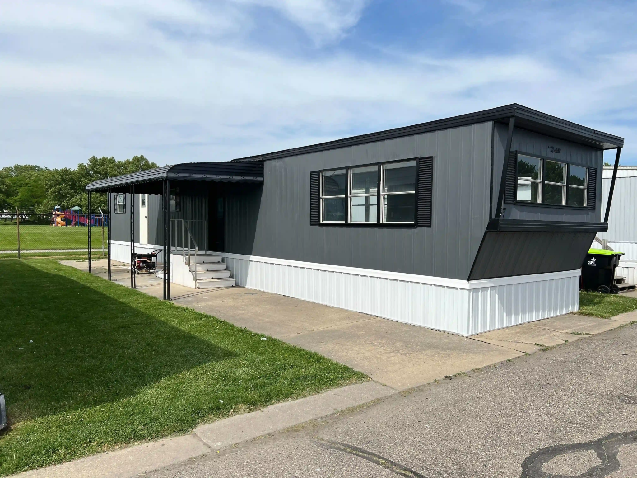 Side view of a modern mobile home with a covered porch and well-maintained surroundings at Roseville Mobile Home Park.