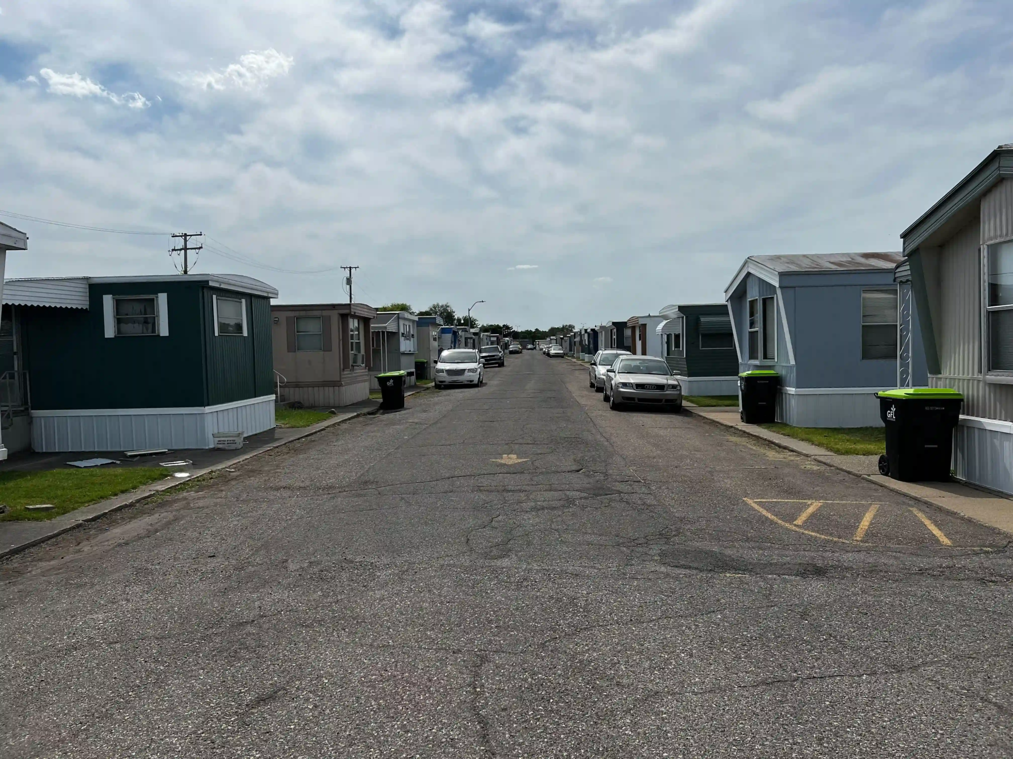 Wide street in Roseville Mobile Home Park with mobile homes on either side, parked cars, and a cloudy sky.