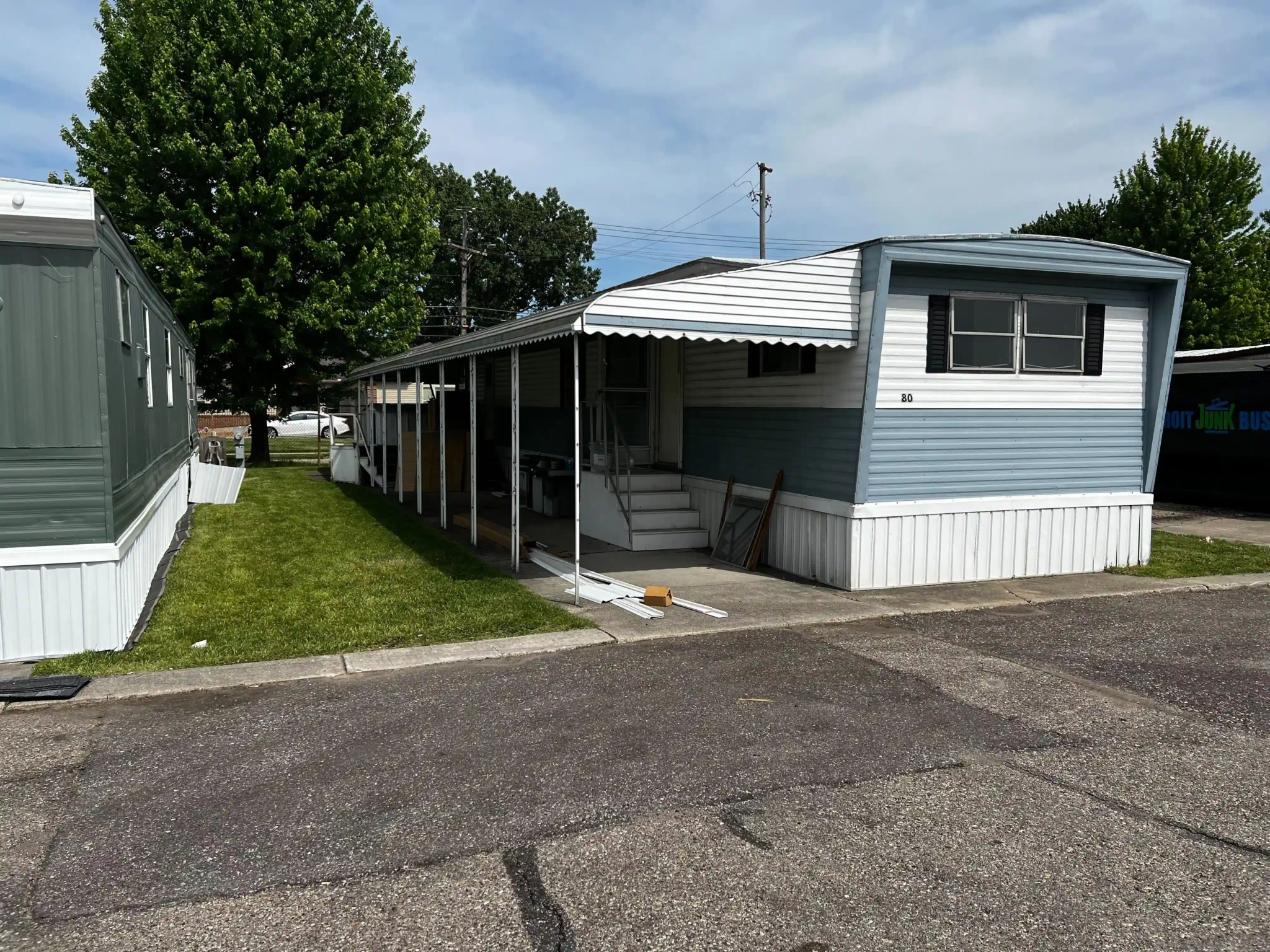 Mobile home with a large front porch and a small lawn area at Roseville Mobile Home Park, under a clear sky.
