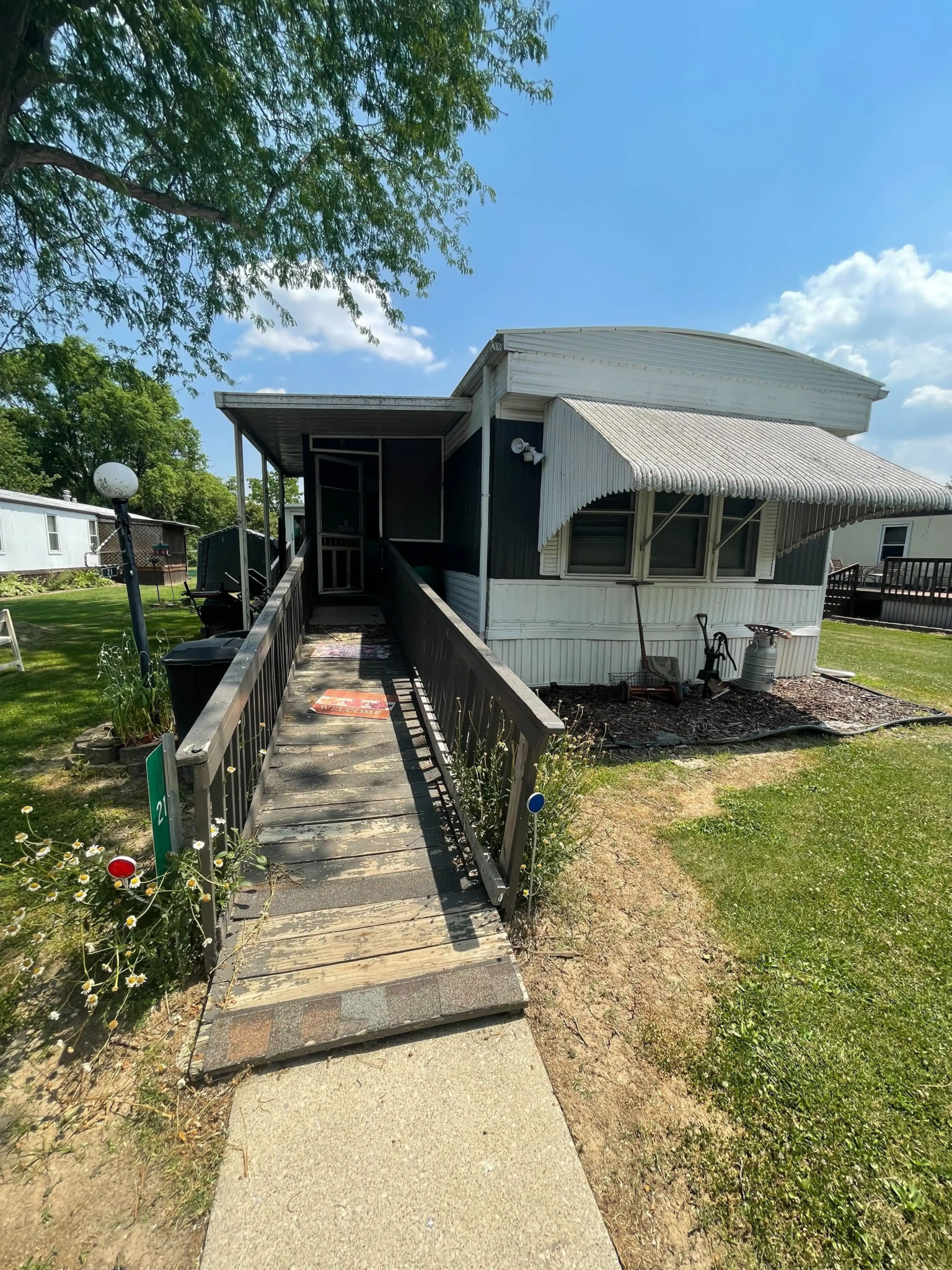 Mobile home with an accessible ramp at Willow Haven Mobile Home Park, surrounded by a well-kept lawn and under a partly cloudy sky.