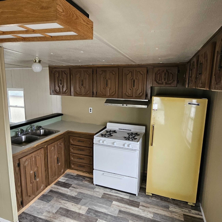 Compact mobile home kitchen featuring a unique yellow refrigerator, white stove, and wooden cabinets, combining functionality with a touch of retro style.