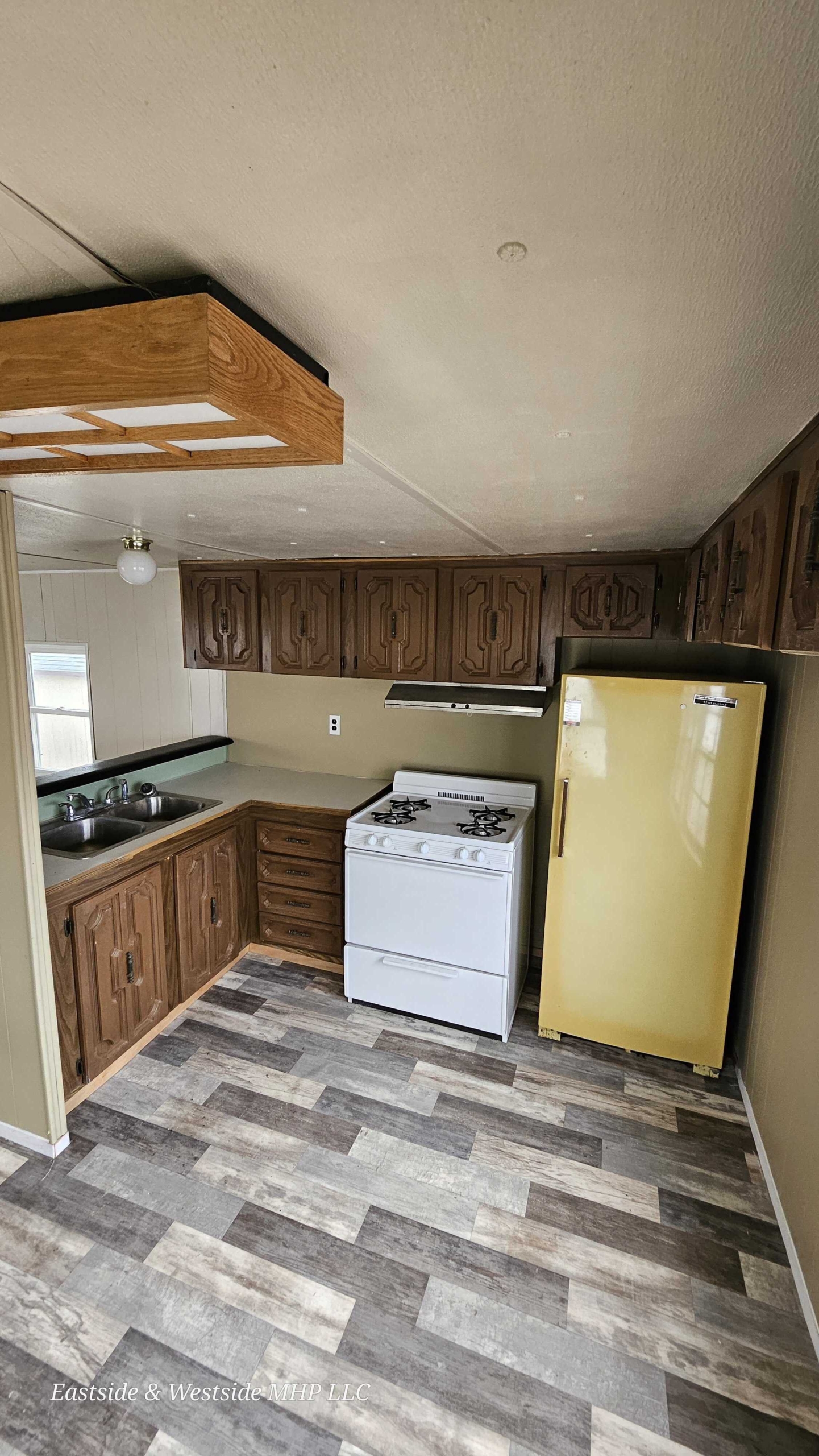 Compact mobile home kitchen featuring a unique yellow refrigerator, white stove, and wooden cabinets, combining functionality with a touch of retro style.