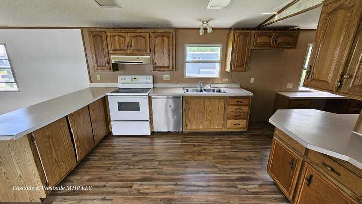 Modern kitchen in a mobile home featuring oak wood cabinets and white appliances, including a refrigerator and stove, set against a faux wood flooring.