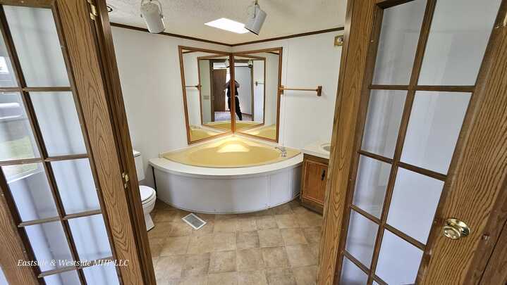 Elegant bathroom in a mobile home showcasing a large corner tub with mirrors and a window, ideal for relaxation and comfort.